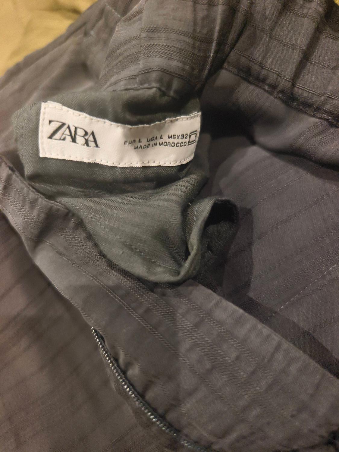 Dark grey fabric Zara clothing label, shows sizes EUR L, USA L, MEX 32, made in Morocco.