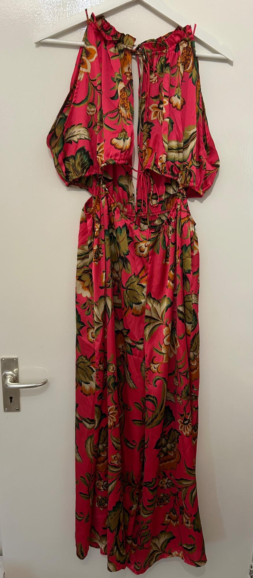 Long dress hanging on a hanger, with a floral print in shades of green and brown on a vibrant pink background.