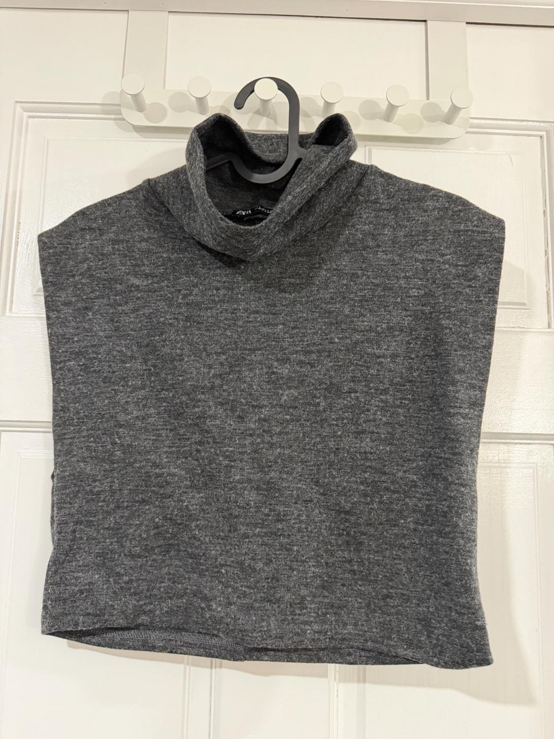 Grey polo neck jumper hanging on a black hanger against a white door background with hooks.