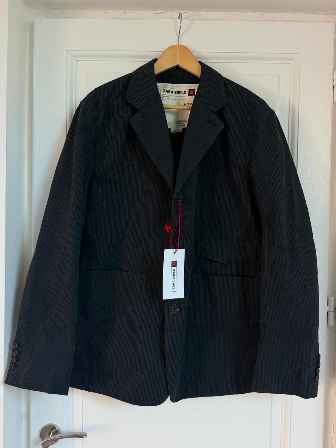 Black fine-striped jacket hanging on a white door, with Zara SRPLS label visible inside and out.