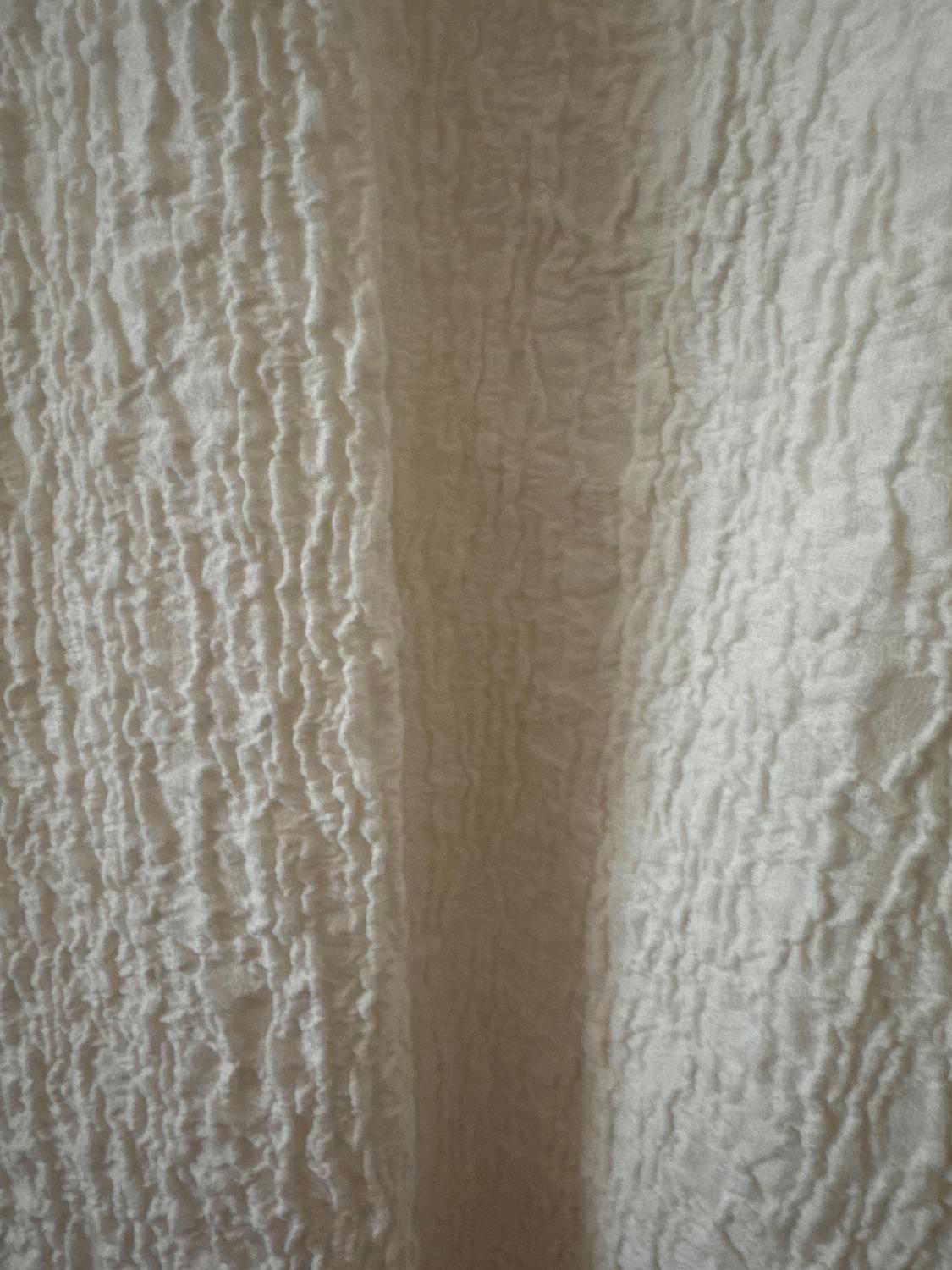 Wrinkled fabric texture in beige tones, with a pattern of vertical folds that create a visual effect of depth.