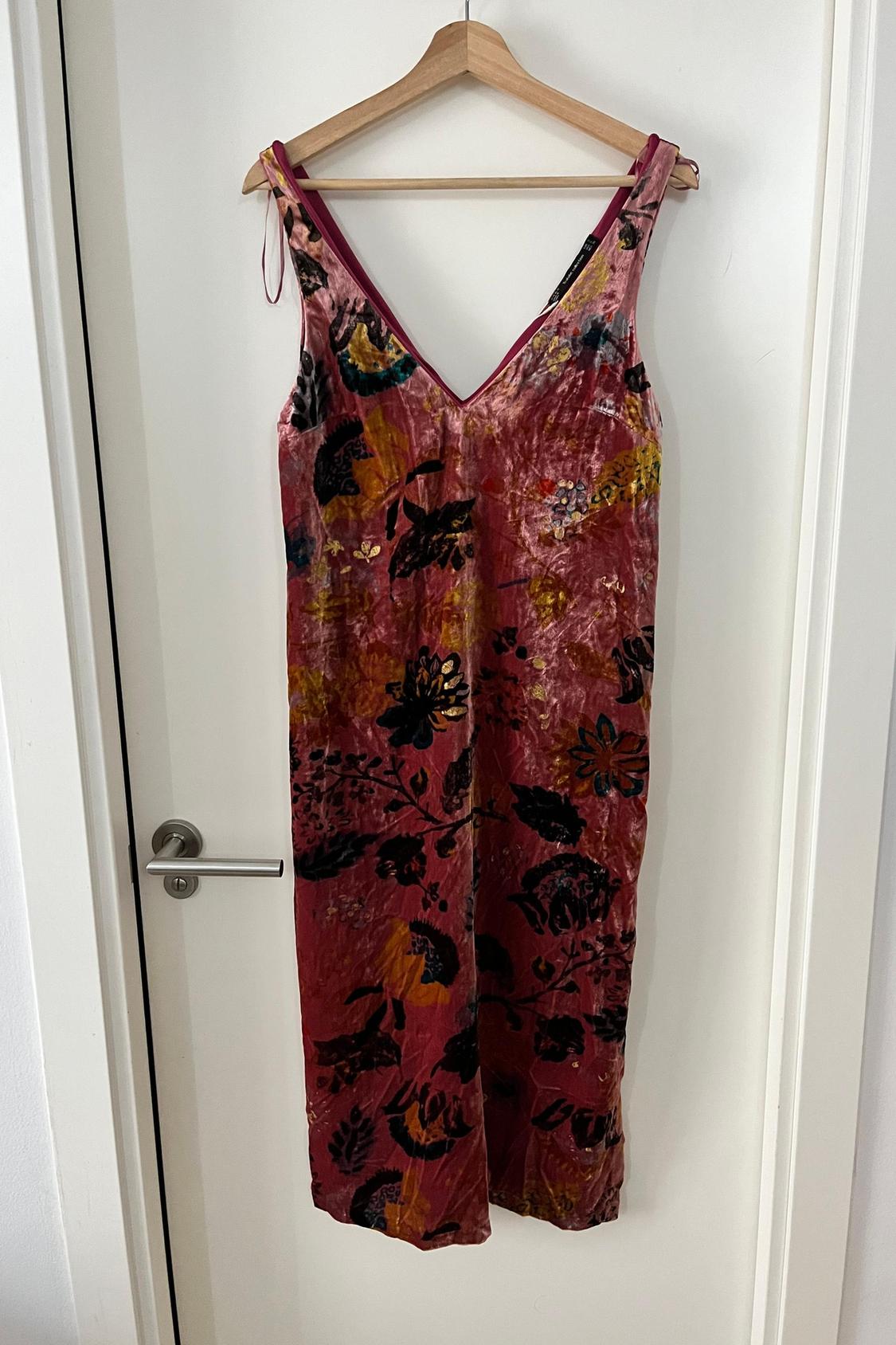 Front view of sleeveless dress with multicoloured floral print on pink background.