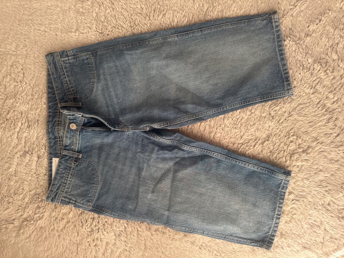 Blue denim shorts with a distressed wash, slightly unbuttoned, resting on a soft, light-coloured rug.