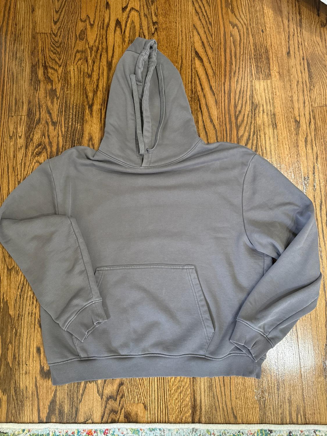 Gray hoodie with a hood, drawstrings, and a front pocket, placed on a wooden floor.
