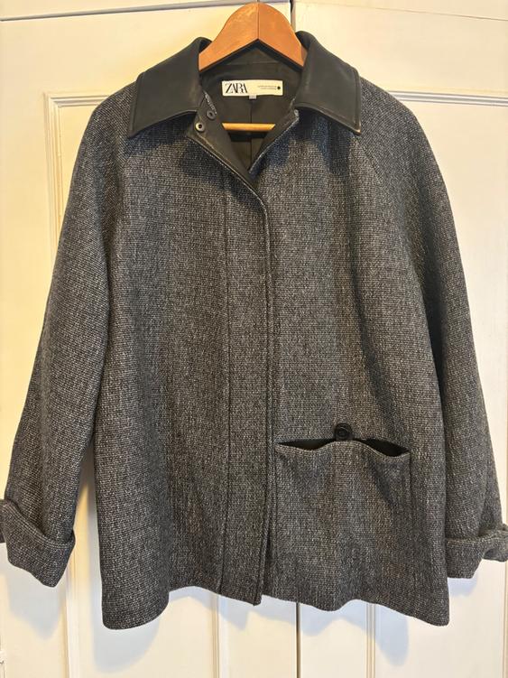 Grey wool coat with a black leather collar, hanging on a wooden hanger. Visible label with the text "ZARA".