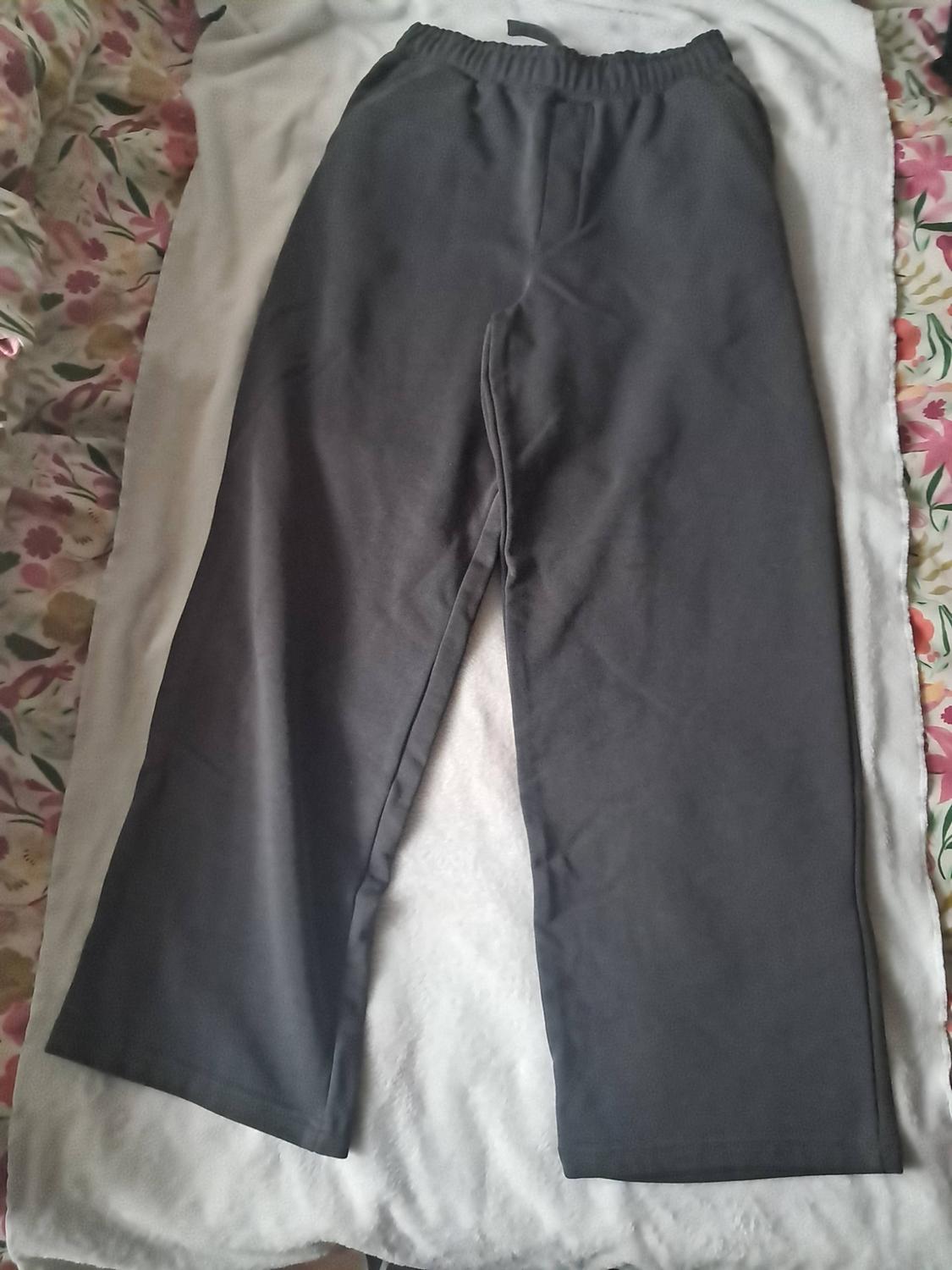 Dark grey trousers with an elasticated waistband and drawstring, laid out on white fabric against a floral-patterned background.