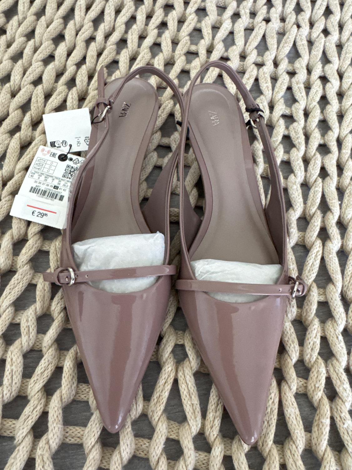 Light brown pointed shoes with straps, on a woven rug. Visible tags with a price of €29.95.