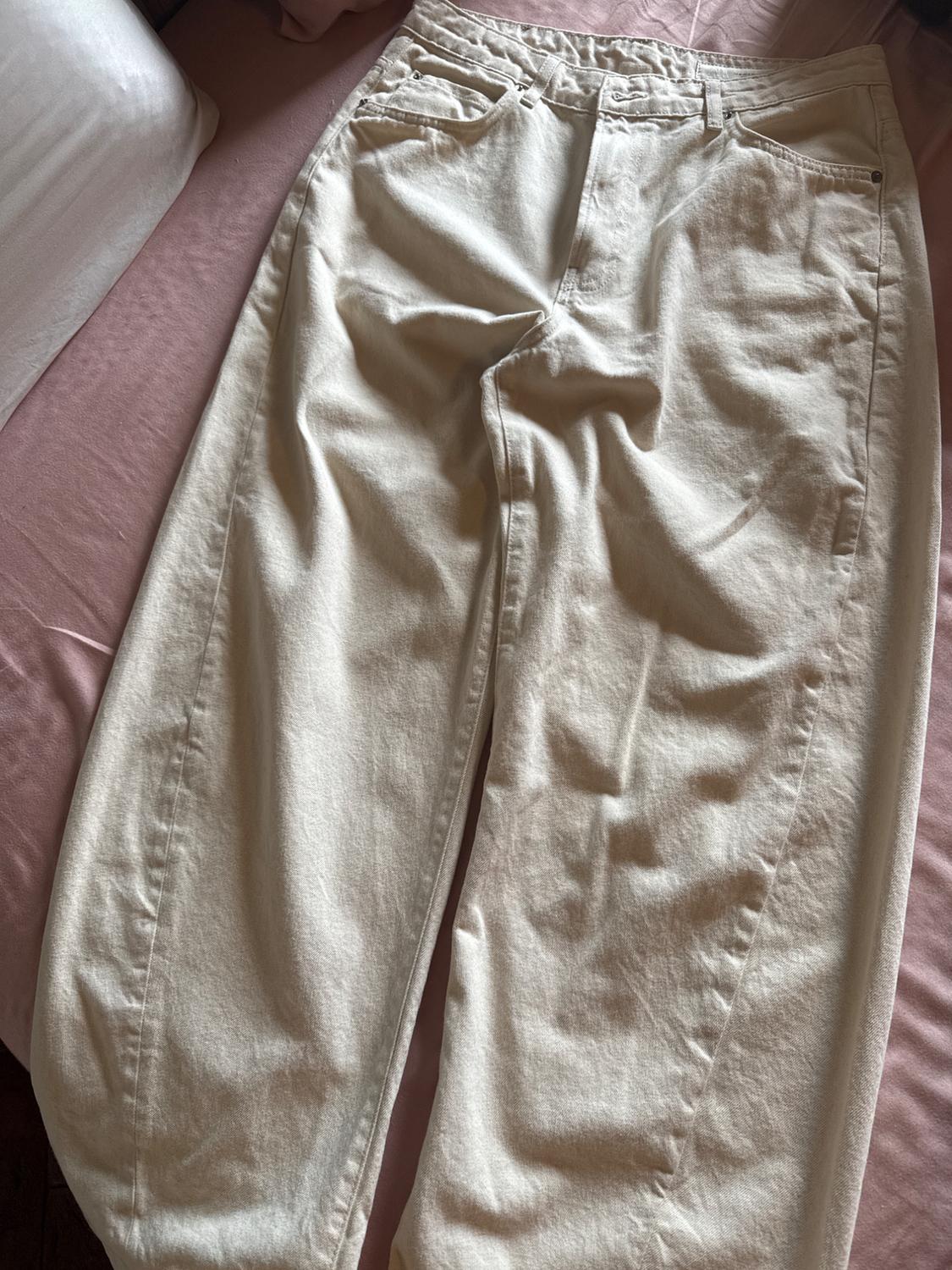Light beige wide-leg jeans laid out on a bed with pink sheets and a white pillow. Casual style.