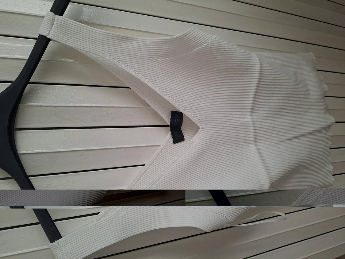 White ribbed vest top hanging on a black hanger against a white wooden slat background.