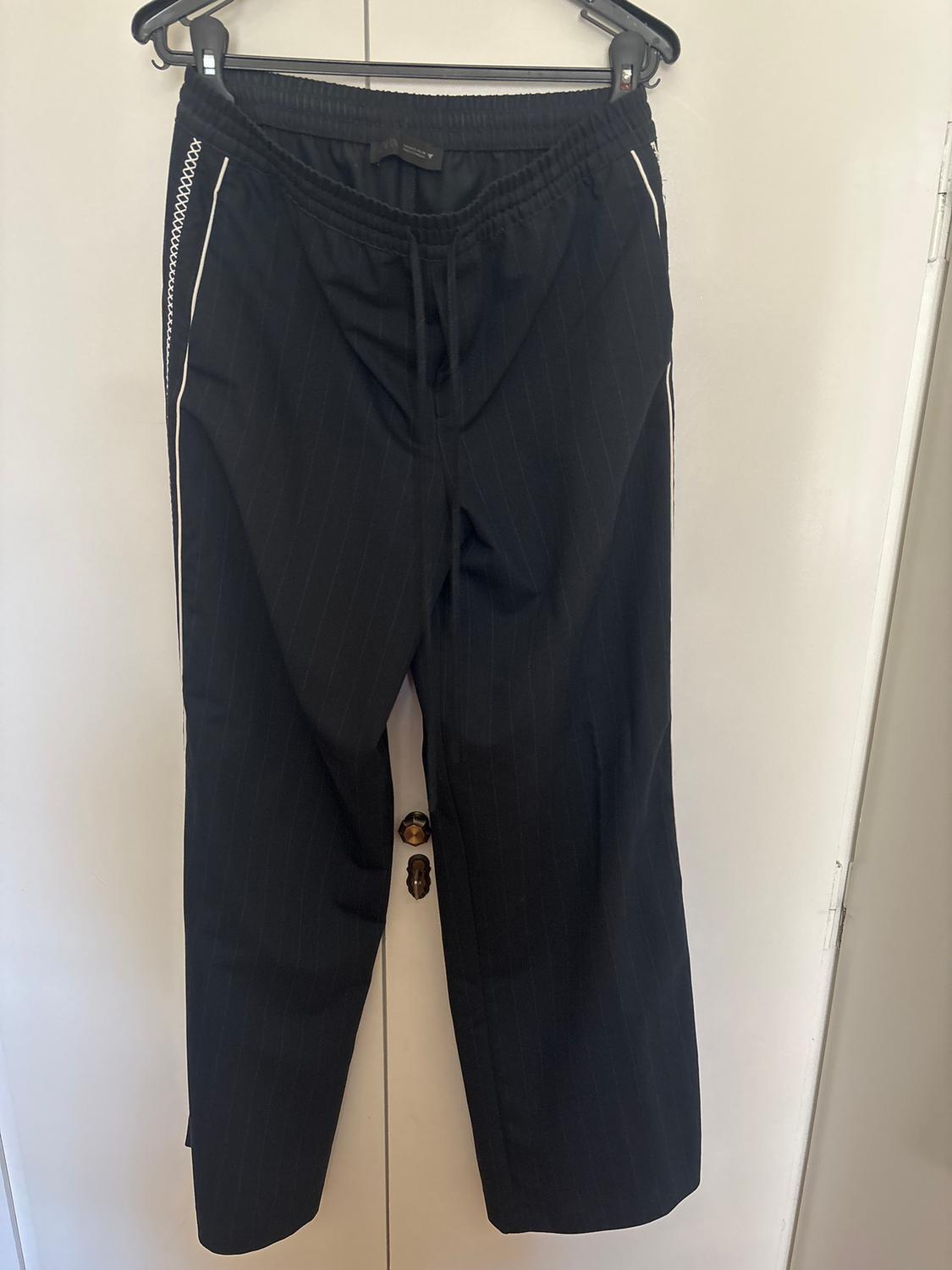 Black striped trousers hanging on a hanger, with an elasticated waist and white detailing on the sides, on a white background.