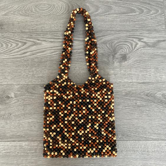 Beaded handbag in shades of brown, beige, and black on a grey wooden floor. Long handle design and dense weave.