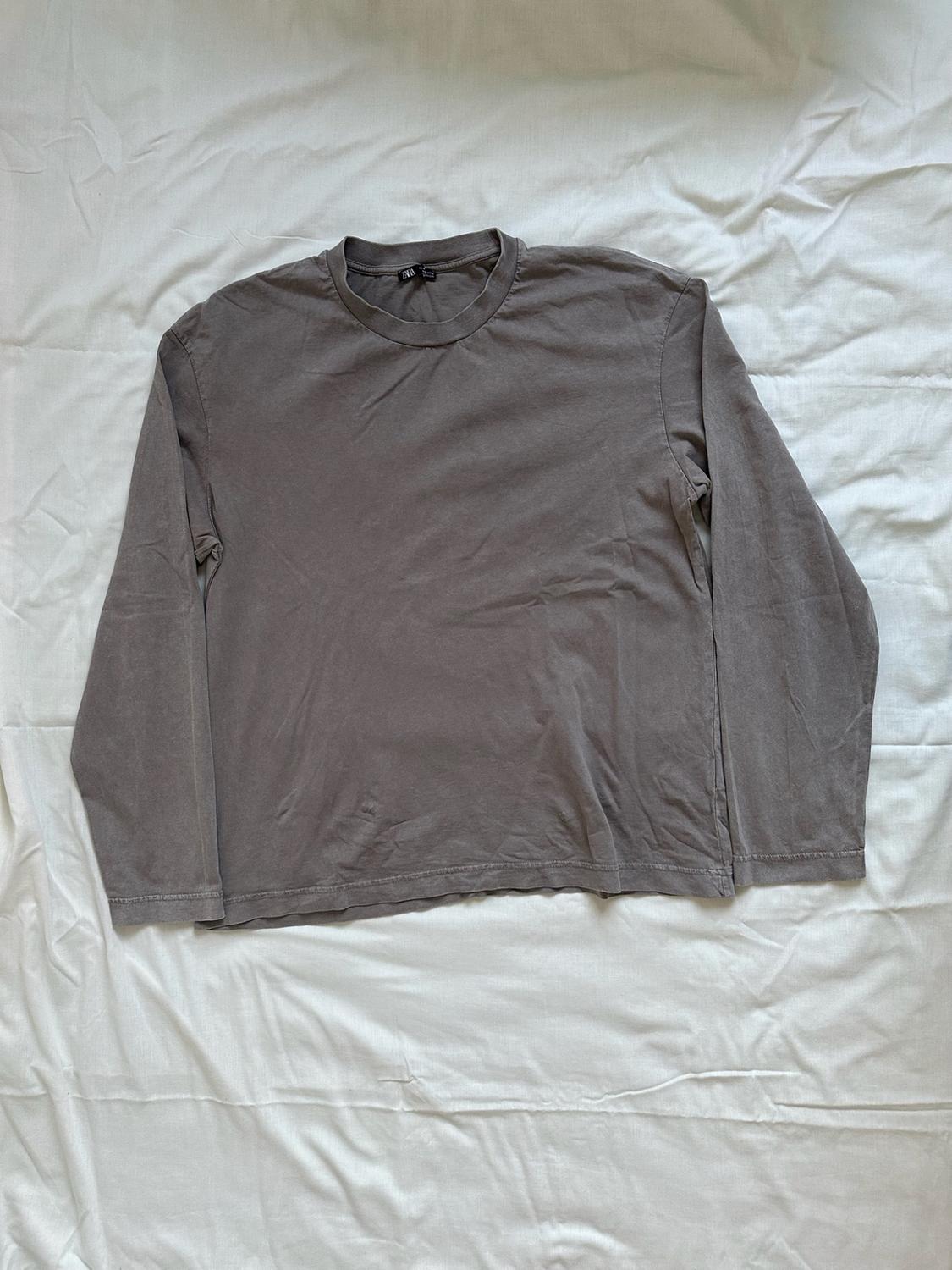 Grey long-sleeved, crew-neck T-shirt laid out on a crumpled white sheet, creating a casual and relaxed atmosphere.