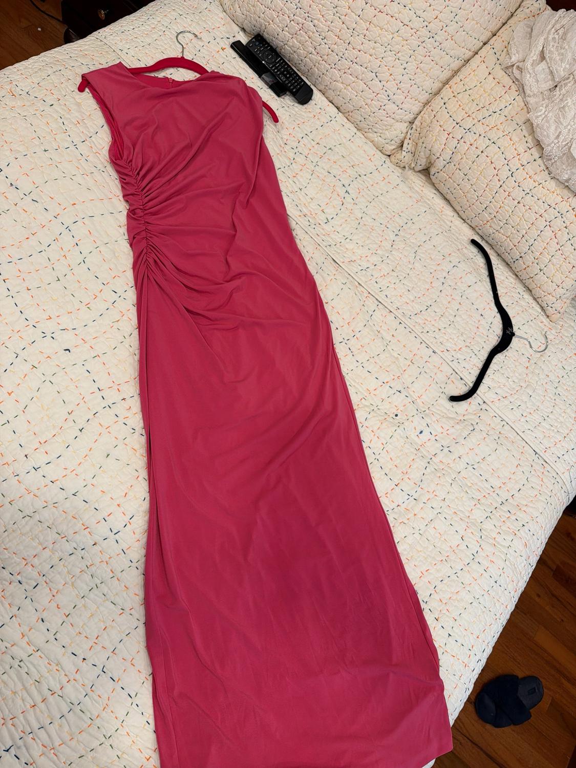 Fuchsia pink maxi dress with side ruching, on a bed with a white quilted bedspread in a relaxed home setting.