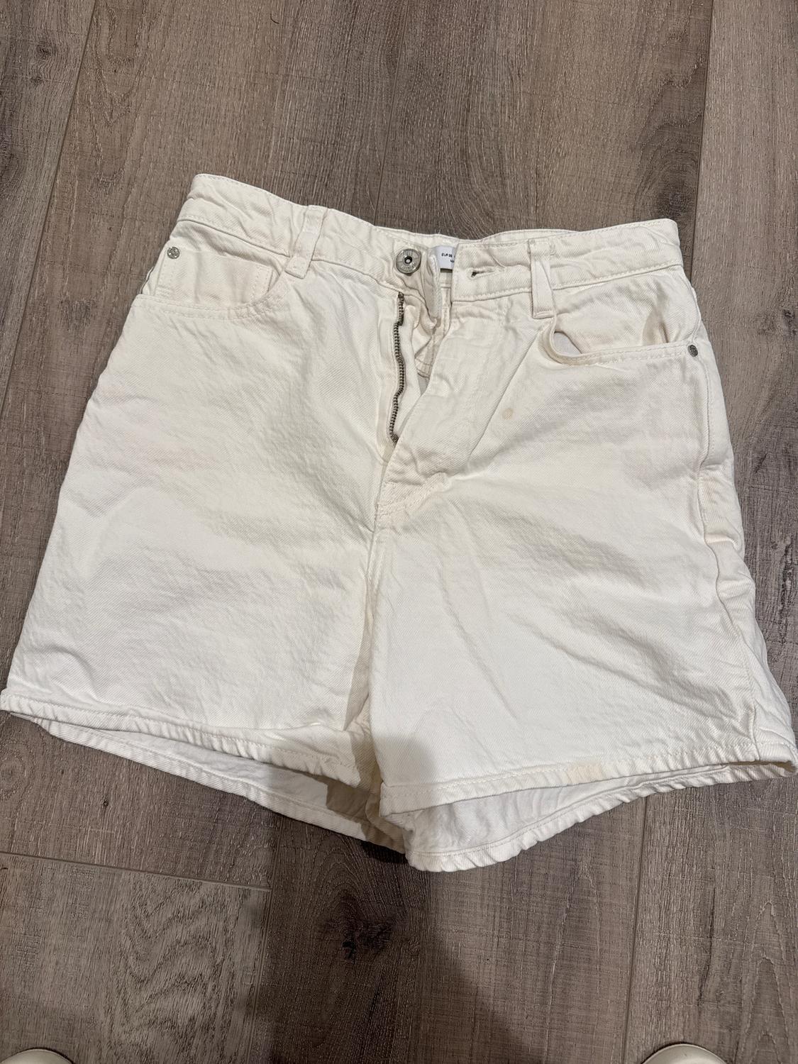 White denim shorts on a brown wooden floor. The zipper is partially open.