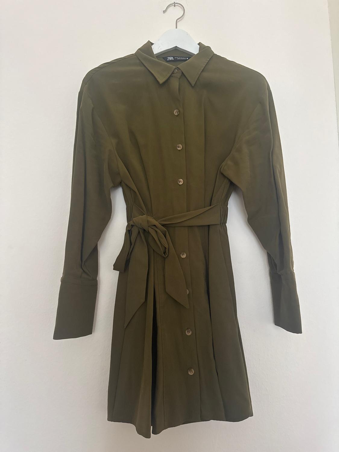 Olive green shirt dress with front buttons and matching belt, hanging on a white hanger against a white background.