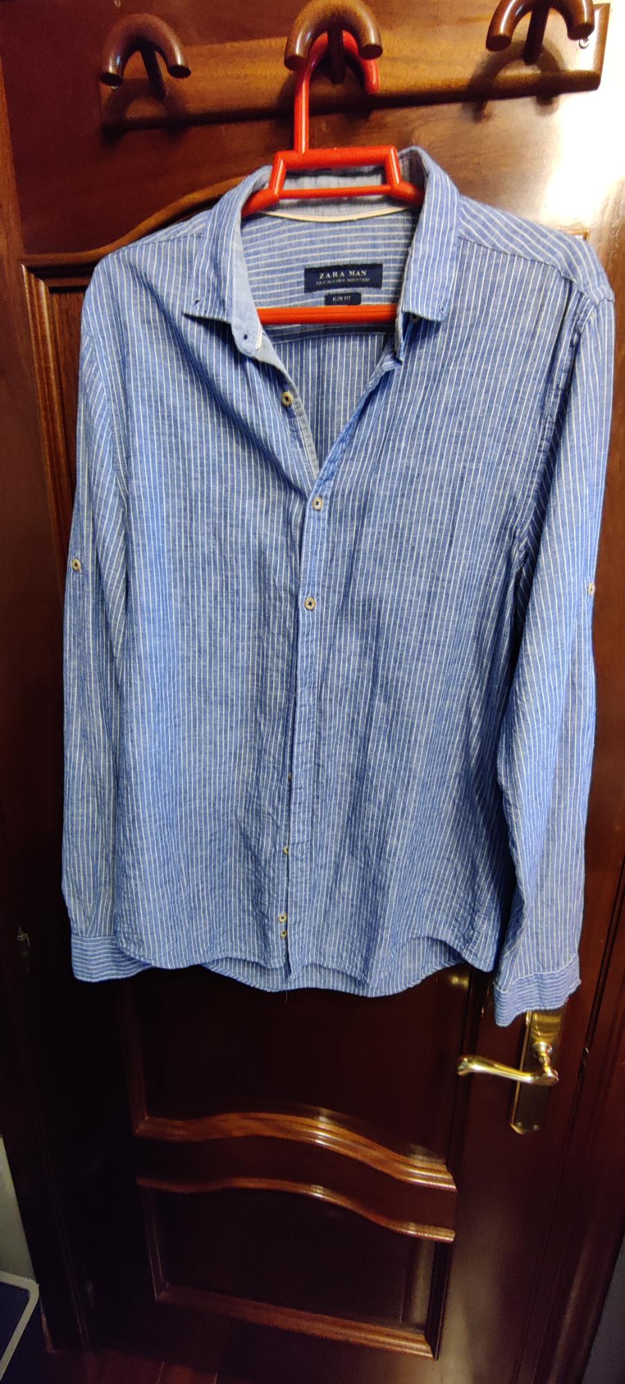 Blue shirt with white stripes hanging on an orange hanger over a wooden door. Label with the text ZARA MAN SLIM FIT.