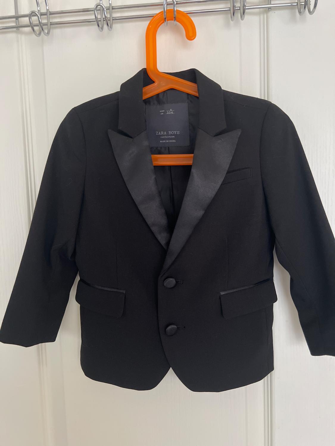 Black jacket on an orange hanger over a white door. Text: SIZE 4 cm 104 ZARA BOYS collection MADE IN CHINA.
