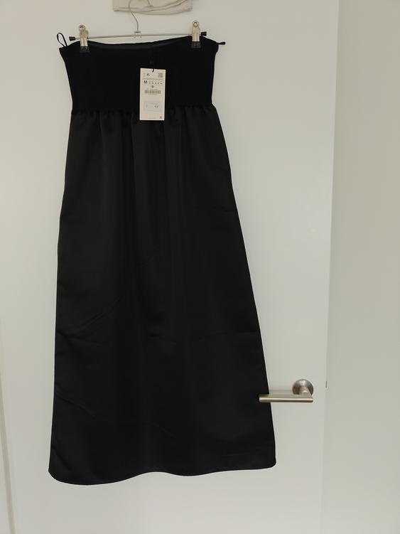 Black dress hanging on a white door with a tag showing size M and a price of 49.99.