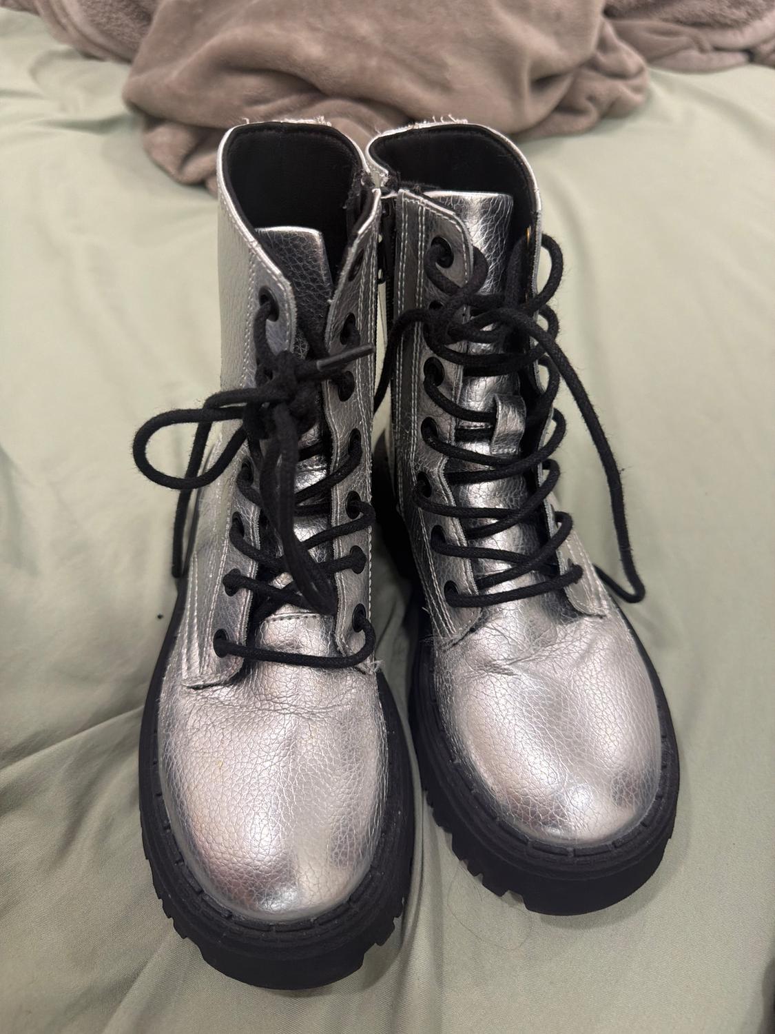 Silver boots with black laces on a green fabric surface. Background with a wrinkled brown blanket.