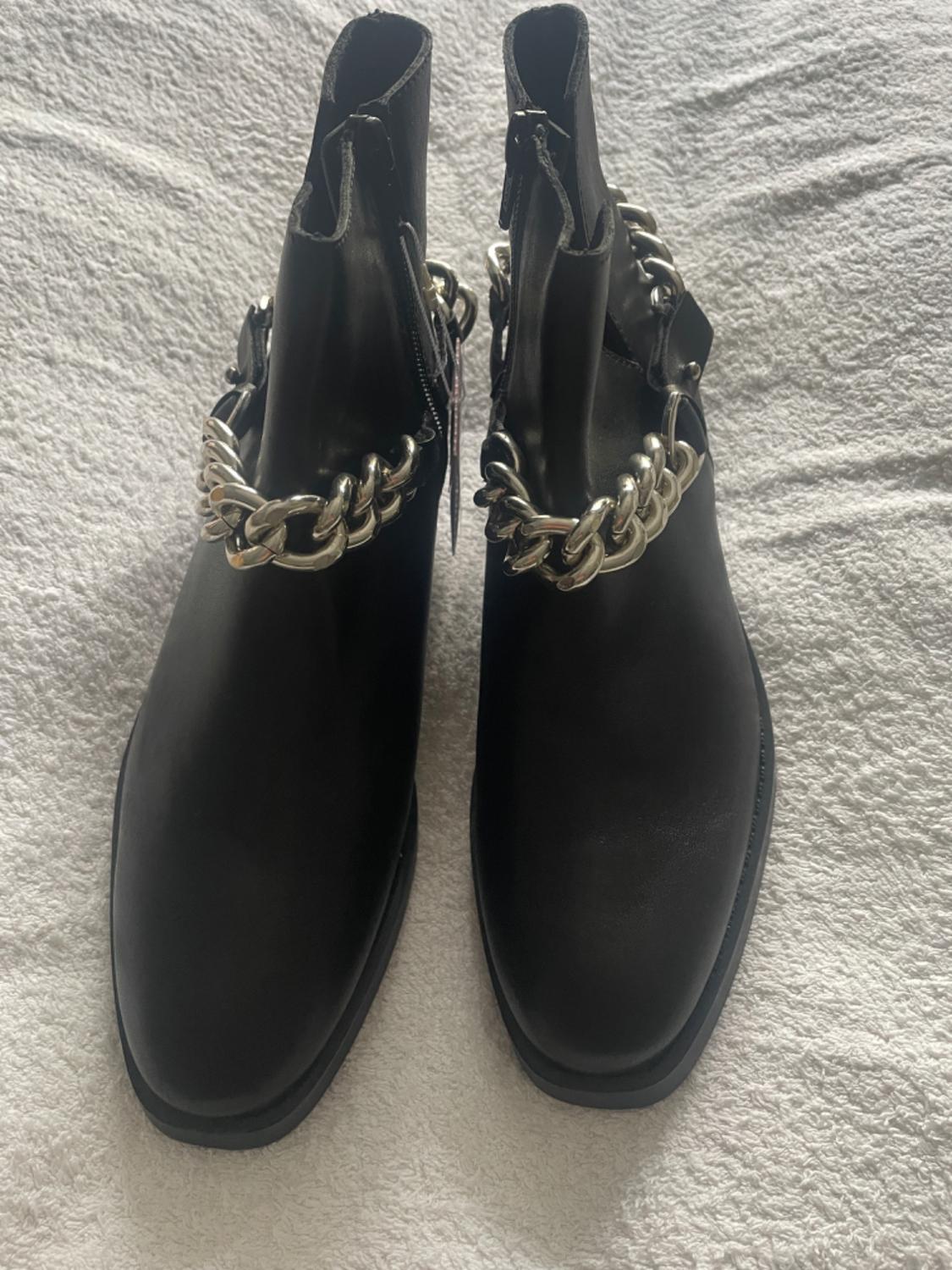 Top view of black boots with a decorative metal chain.