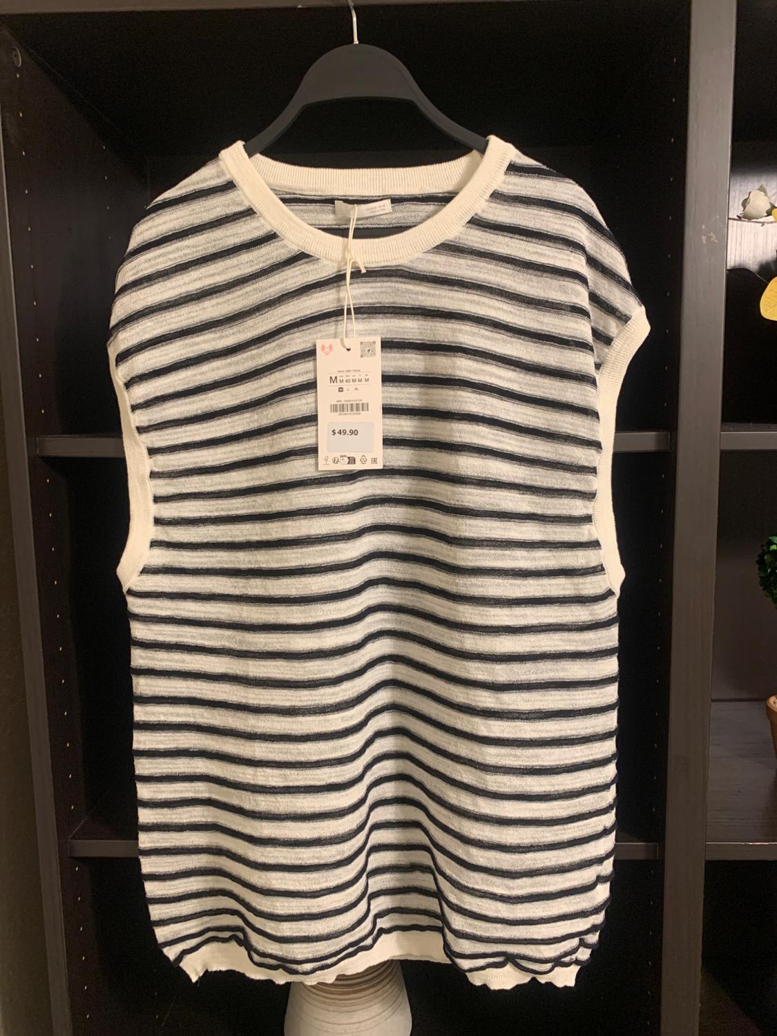 Black and white striped waistcoat hanging on a black hanger, with a price tag of $49.90, on a dark shelf.
