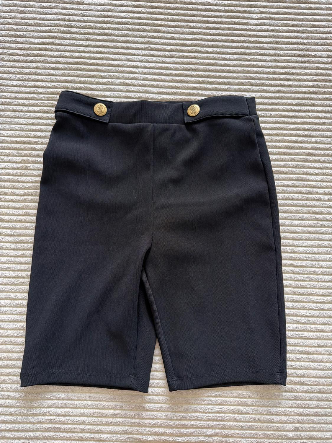 Black shorts with two gold buttons at the waist, against a light ribbed fabric background.