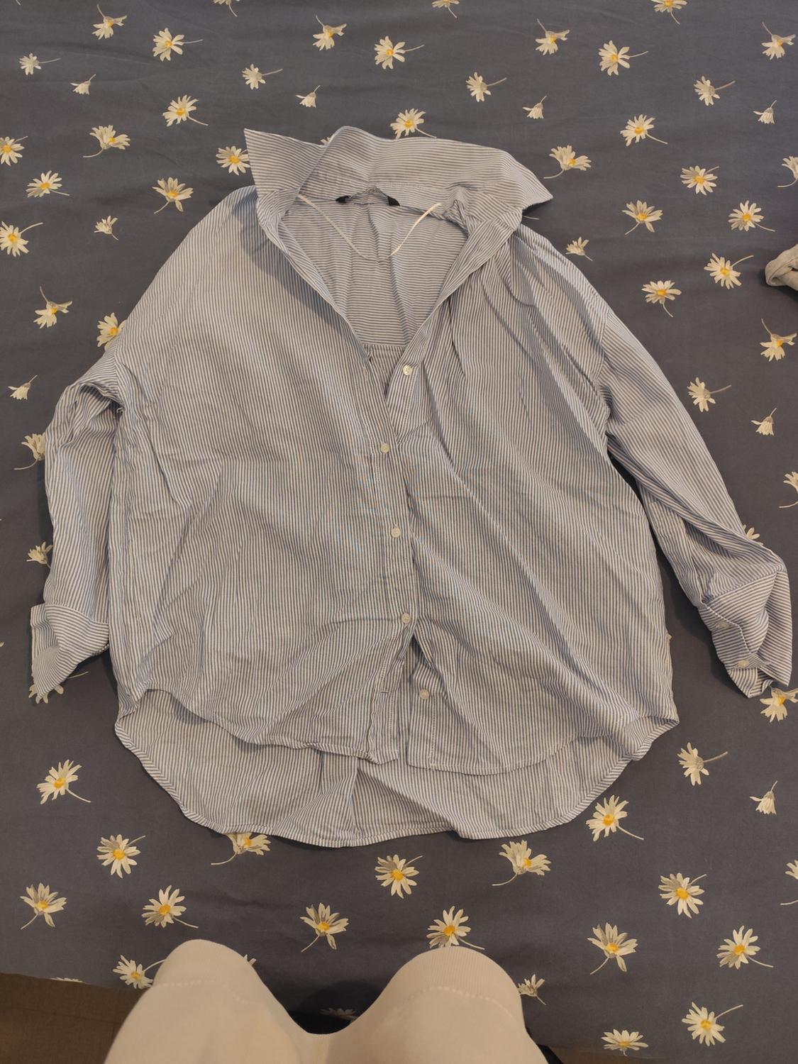 Blue and white striped shirt on a bed with a daisy bedspread. Bottom of beige trousers visible.