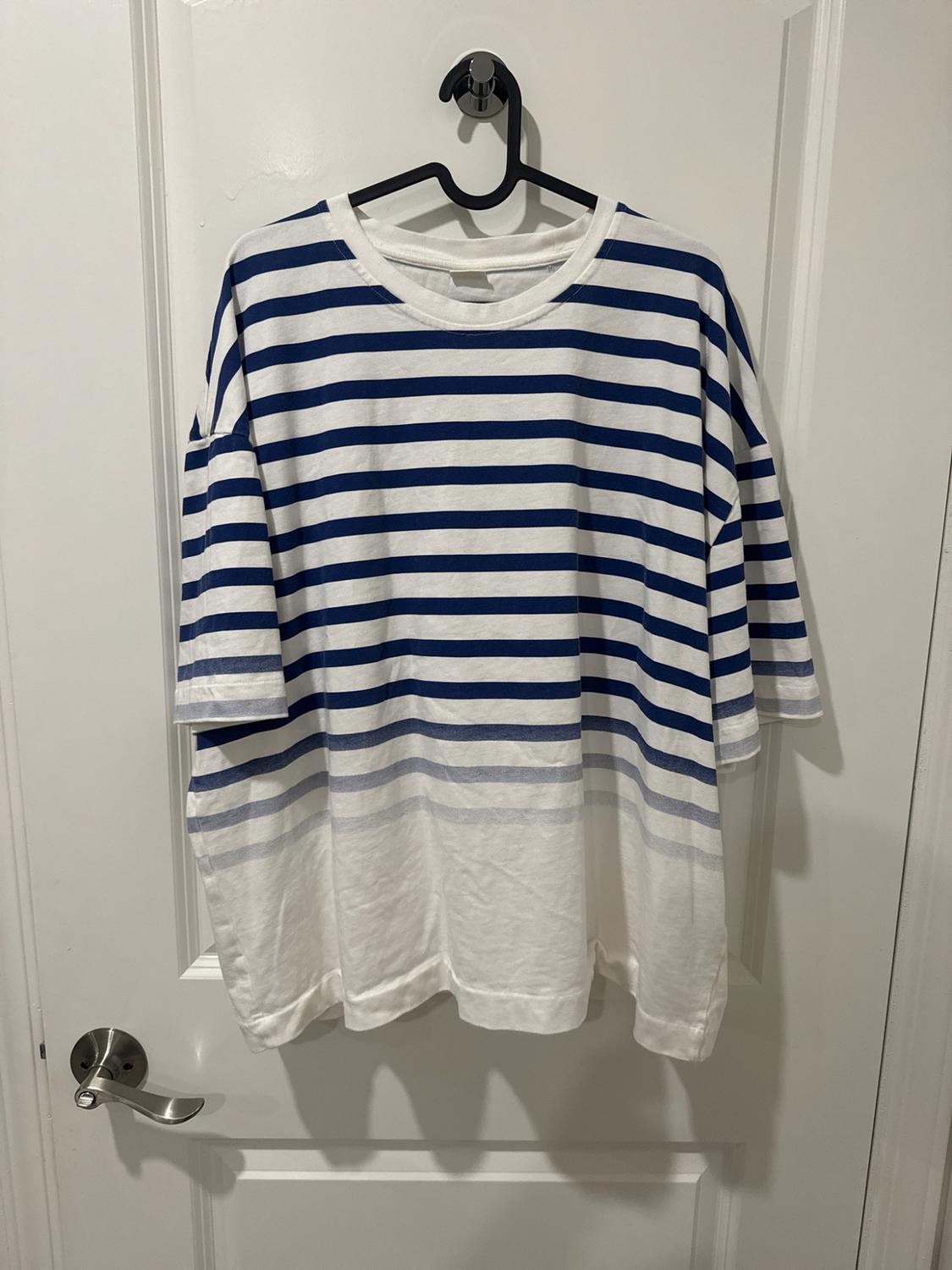 White short-sleeve T-shirt with blue horizontal stripes that fade downward, hanging on a white door.