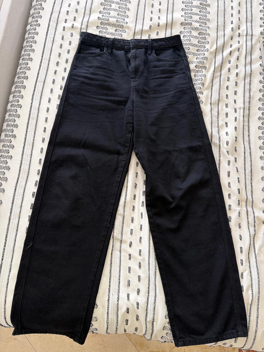 Black straight-leg jeans on a white blanket with black stripes. Relaxed, casual style composition.