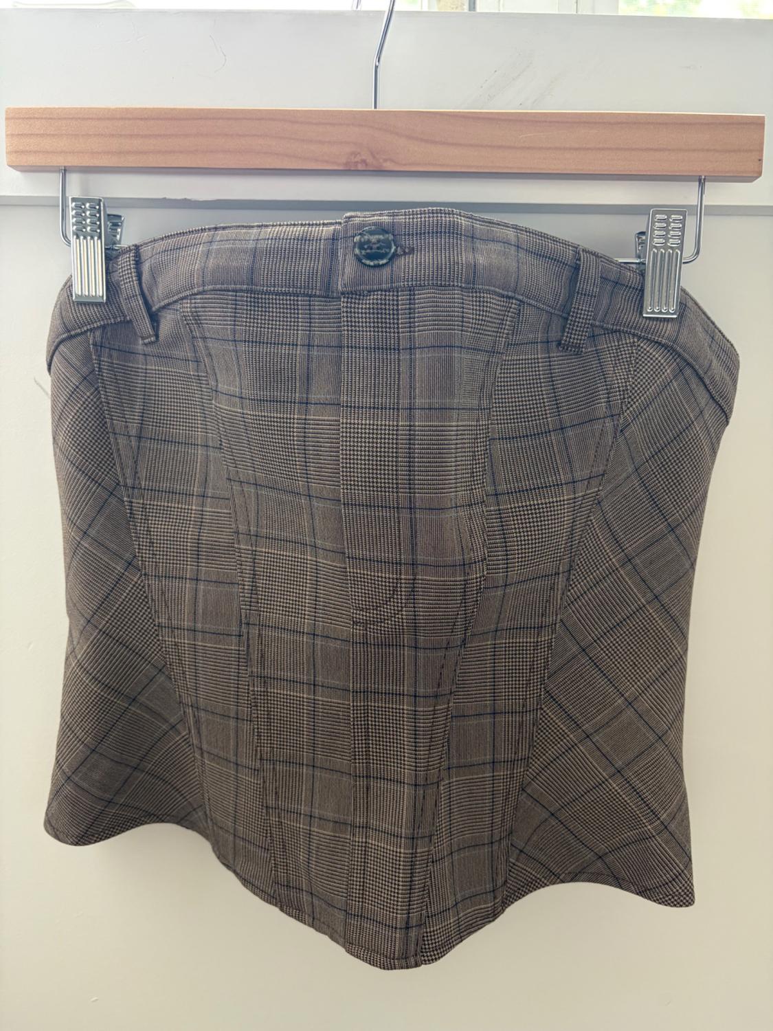 Brown checked strapless corset top with button and belt loops, hanging on a wooden hanger with clips against a white background.
