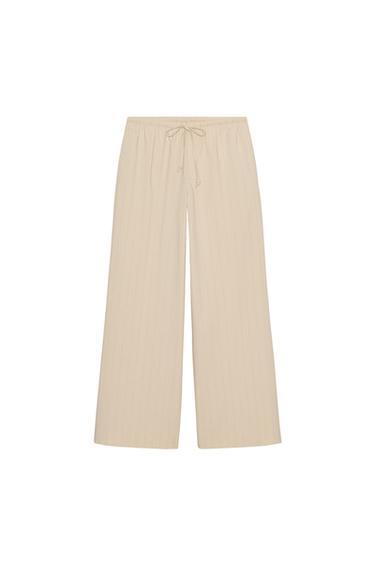 Front view of beige striped pyjama trousers, elasticated drawstring waist and concealed side pockets, wide leg.