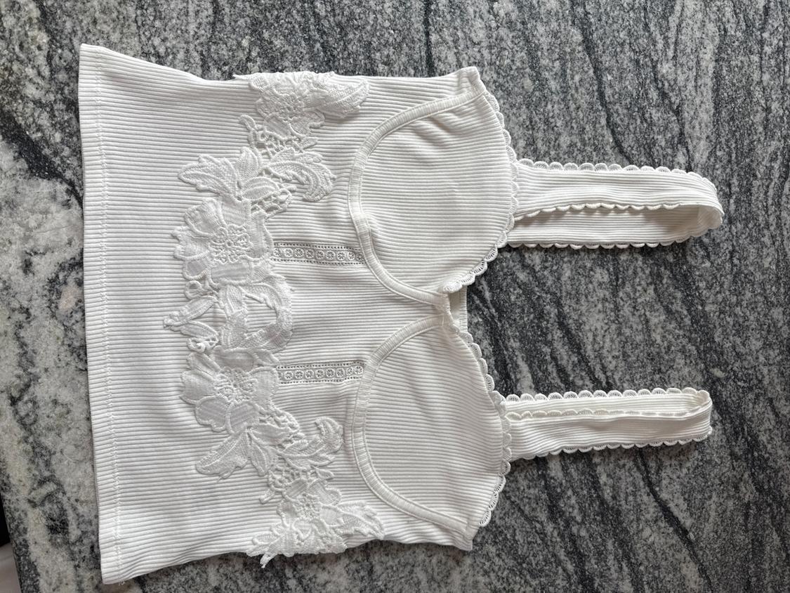 White cami top with floral lace on a grey marble background. Ribbed design with delicate detailing on the straps.