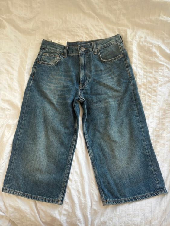 Light blue denim wide-leg jeans on a textured white bedspread. Label visible on the waistband.