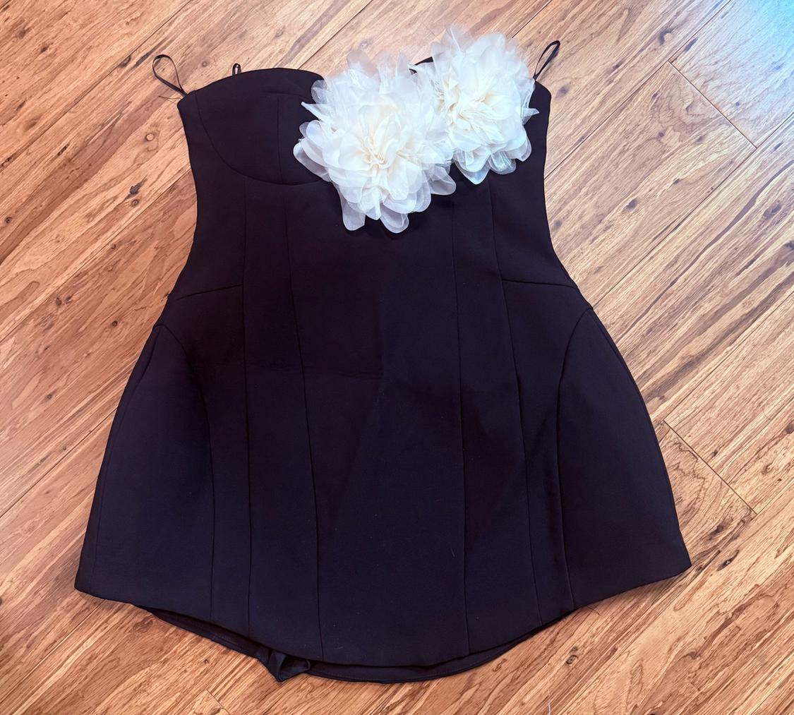 Black crop top with two large white floral details on the neckline, laid flat on a wooden floor.