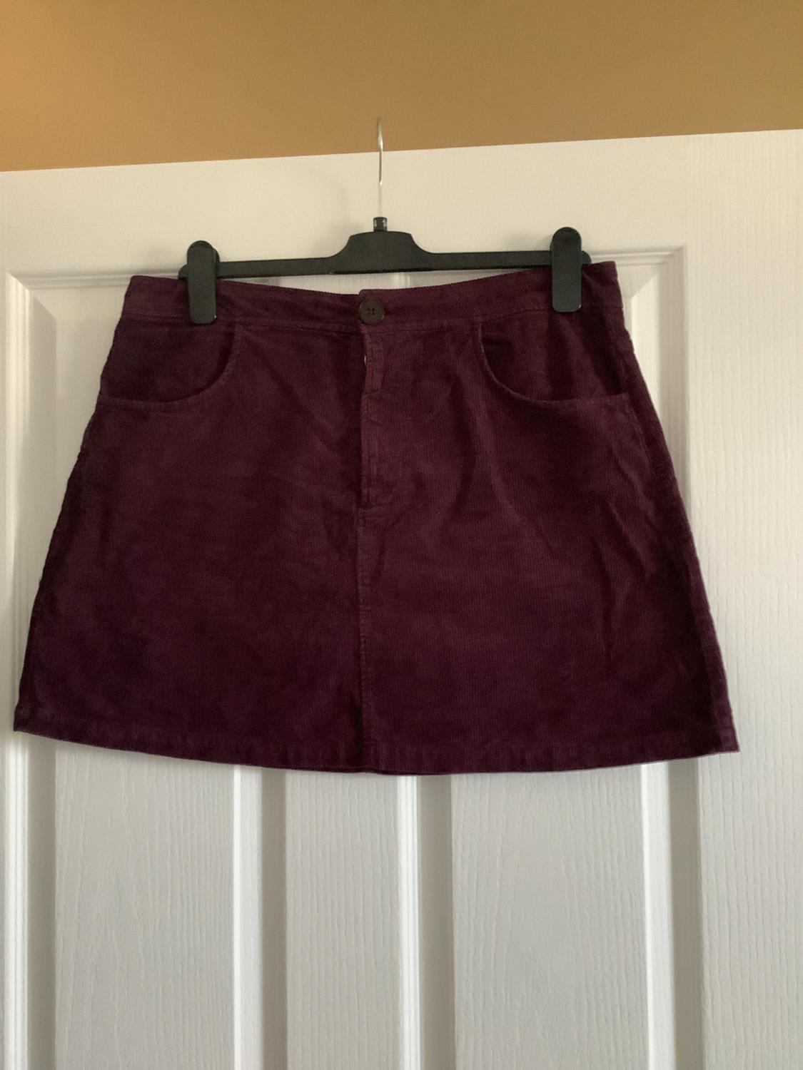 Burgundy corduroy miniskirt hanging on a black hanger over a white panelled door.