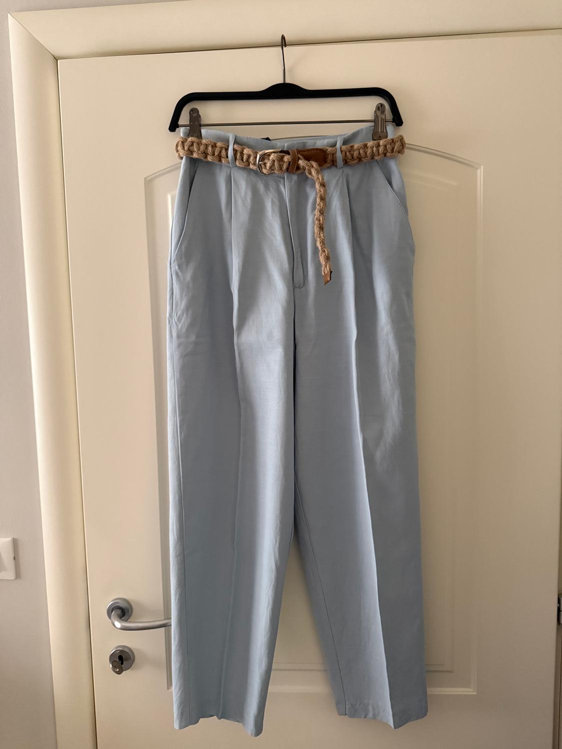 Light blue trousers hanging on a black hanger over a white door, with a light brown braided rope belt.