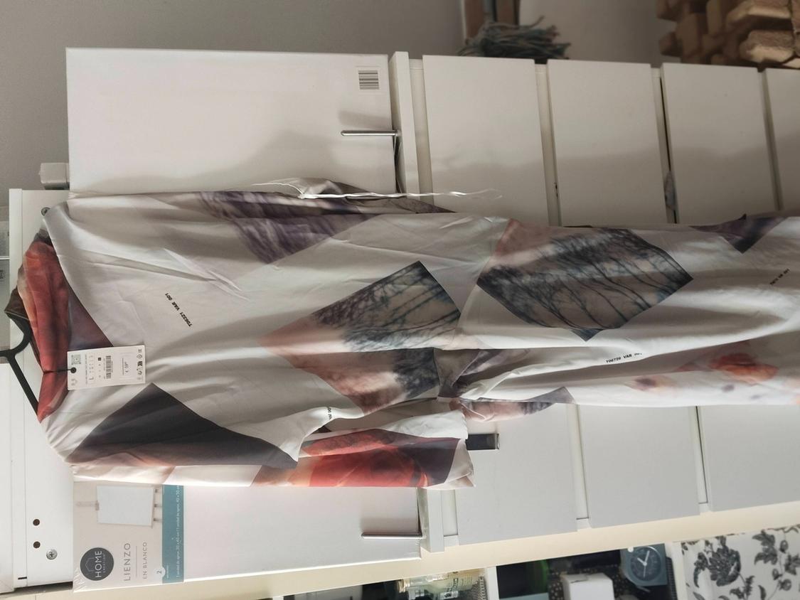 Light-coloured dress with an abstract print hanging in front of a white chest of drawers. Text: HOME BLANK CANVAS.