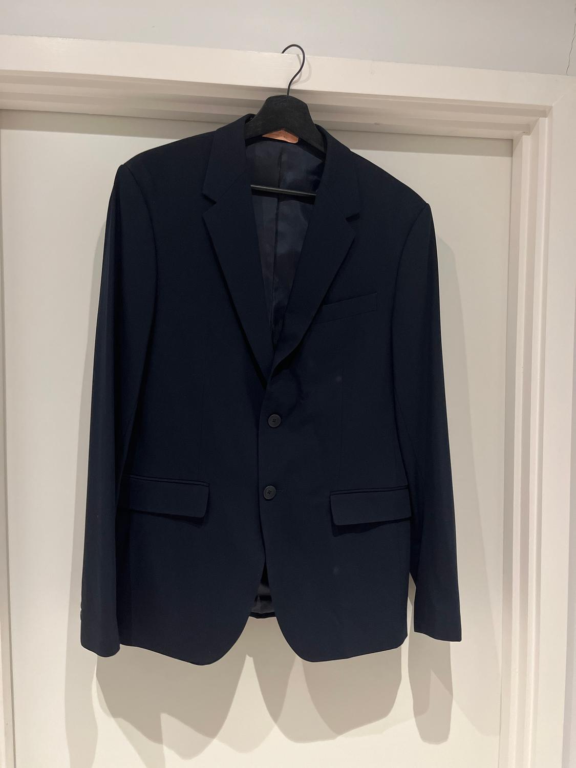 Black suit jacket hanging on a hanger over a white door. The jacket has two buttons and classic lapels.