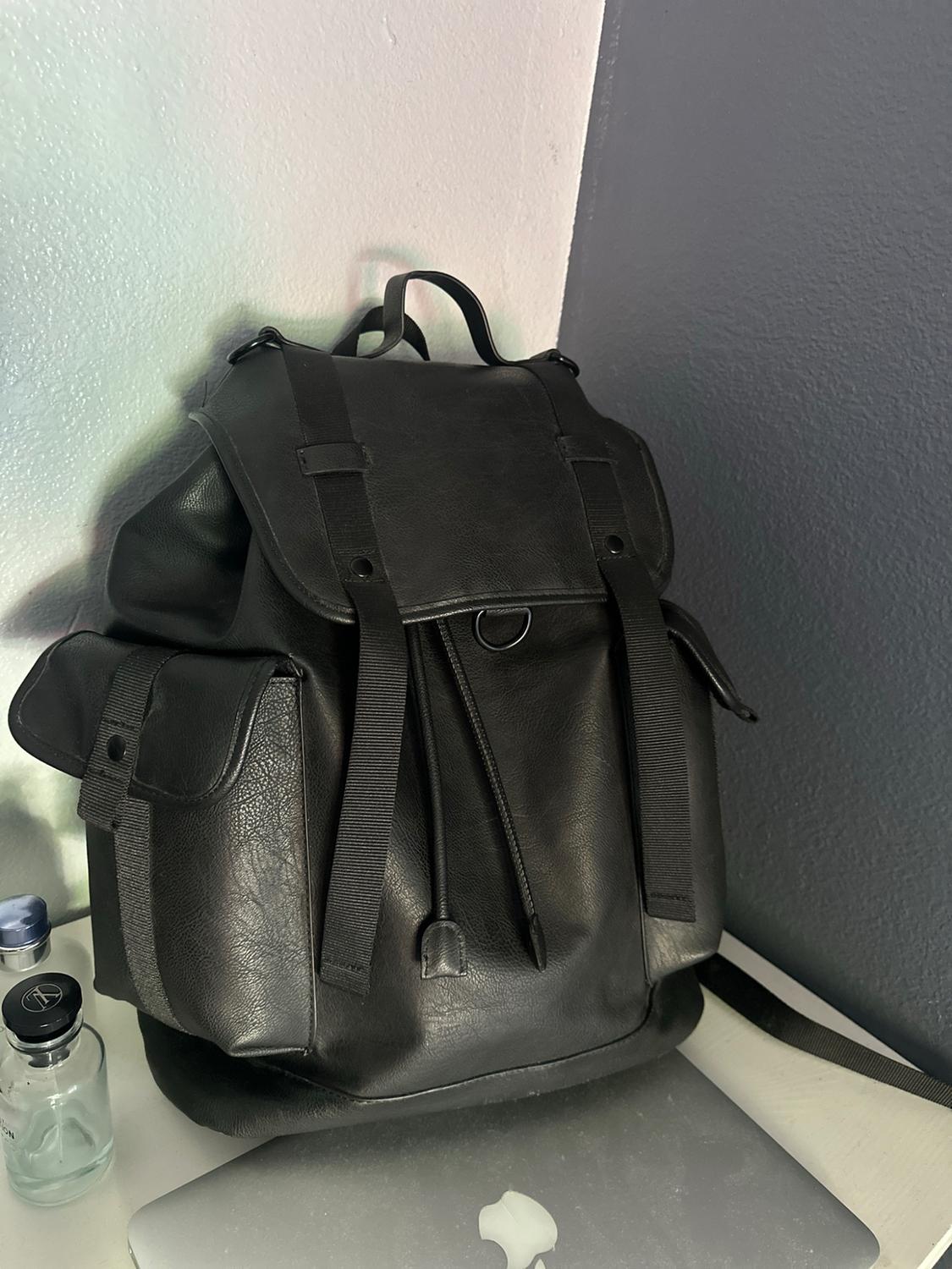 Black backpack with a flap, front straps and side pockets, resting on a silver laptop next to some glass jars.