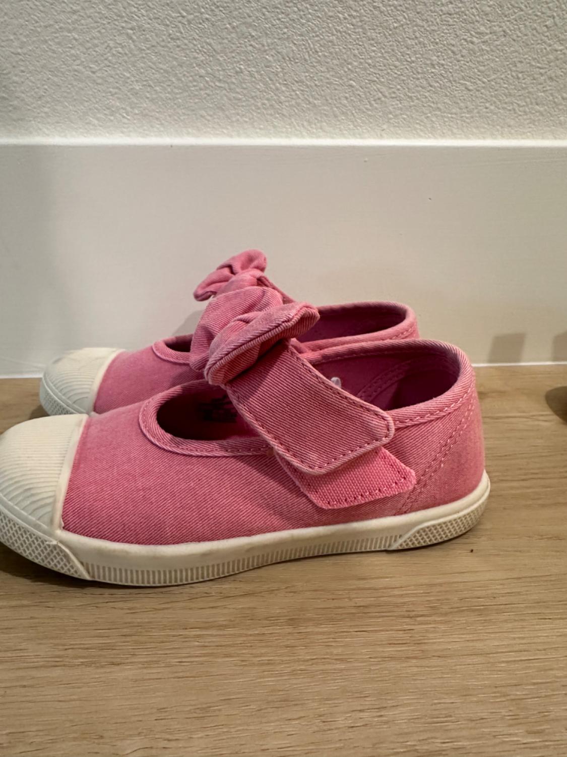 Side view of pink trainers with a bow and white toe.