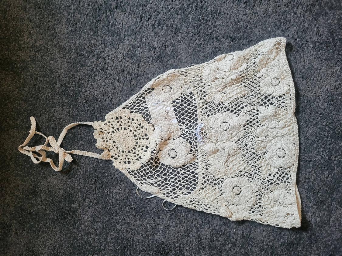 Beige lace top with floral design on a dark grey background. Openwork fabric detail and thin straps.