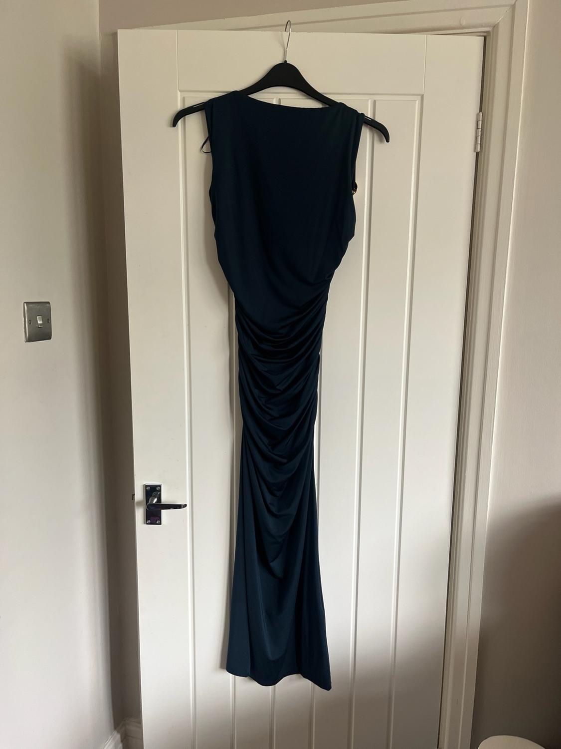 Navy blue sleeveless gathered maxi dress, hanging on a black hanger on a white door indoors.