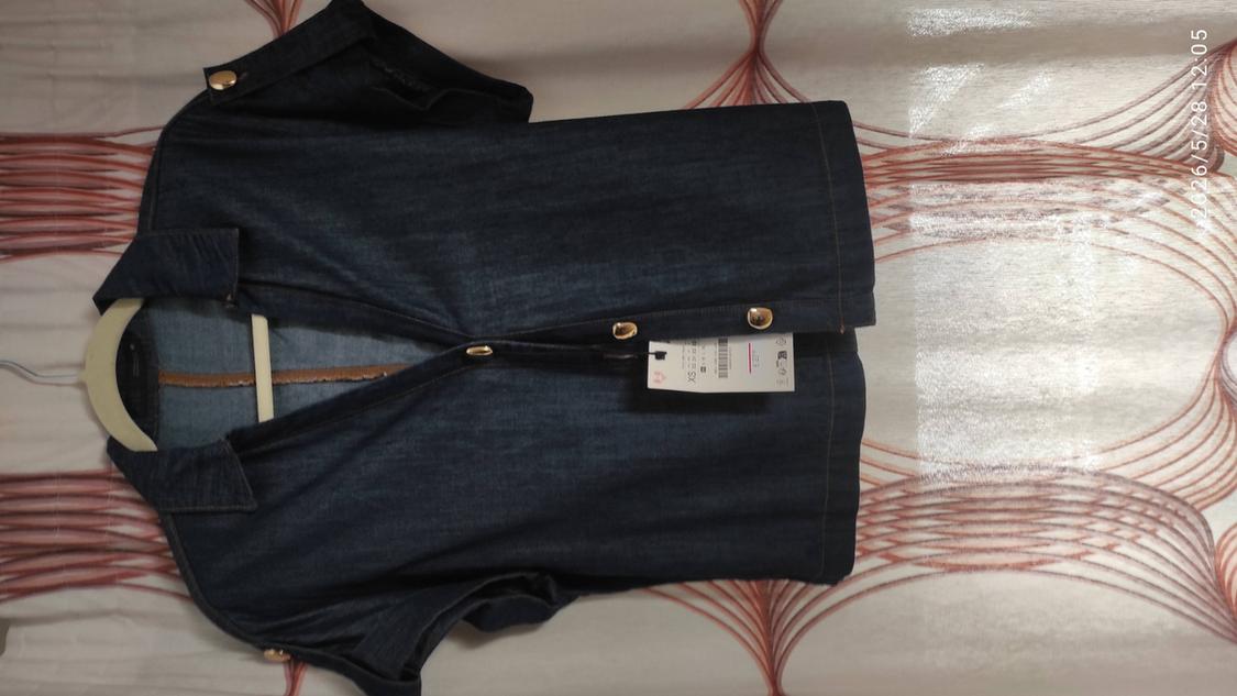 Dark blue, short-sleeved denim shirt with gold buttons on a bed with patterned sheets. Text: 2026/5/28 12:05 XS.