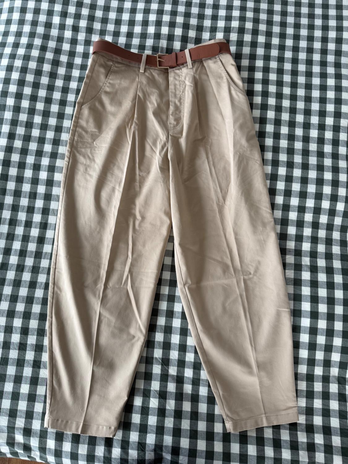 Beige trousers with a brown belt on a white and green checked tablecloth.