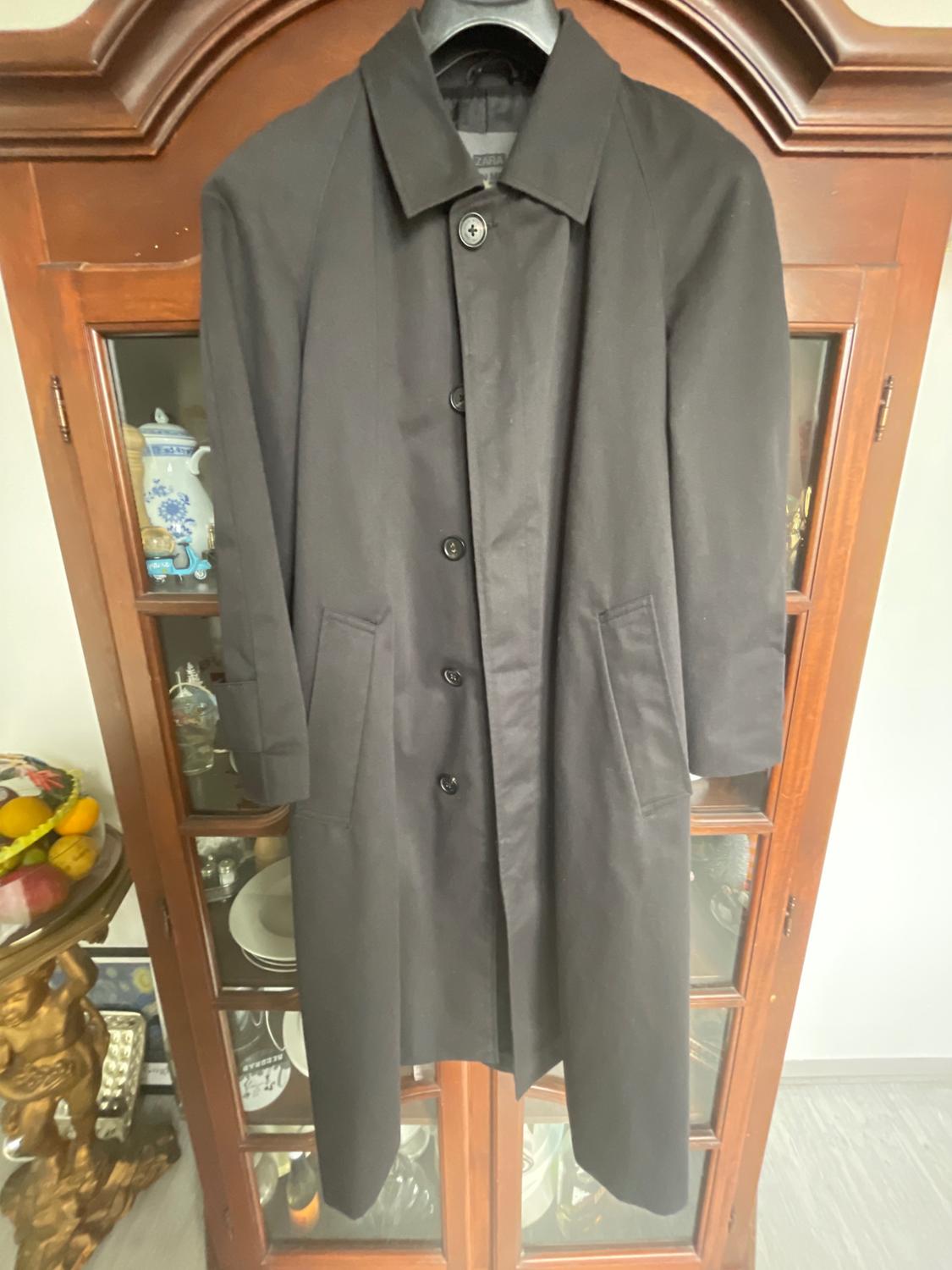 Black coat hanging on a hanger in front of a wooden cabinet with glass doors, displaying tableware and decoration inside.