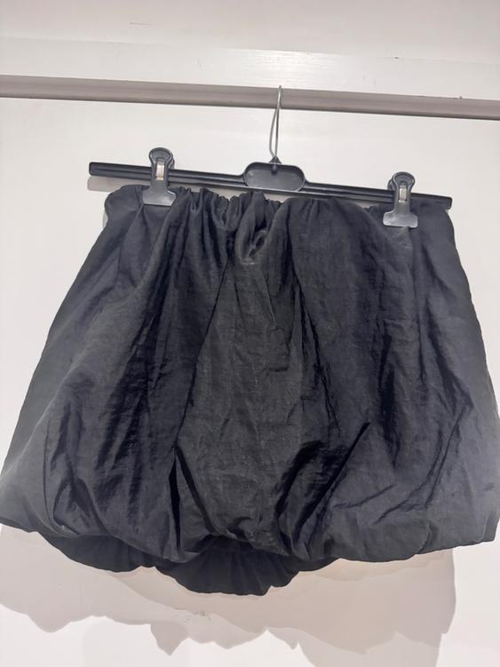 Black skirt with a crinkled texture, hanging on a black hanger against a white background.