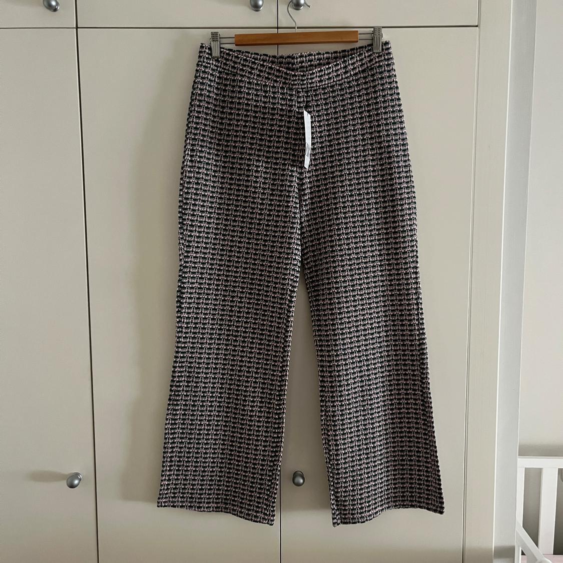 Patterned fabric trousers hanging on a hanger above a white wardrobe. Small checked design in dark tones.