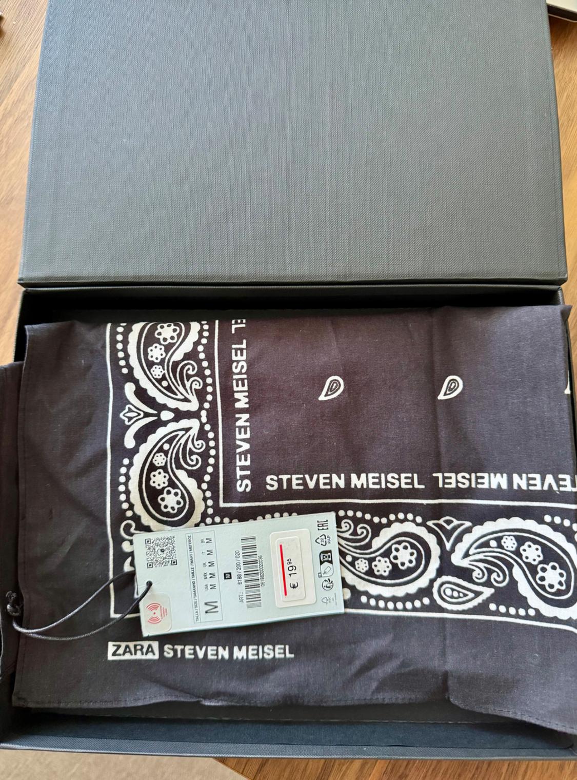 Open box with black paisley design scarf and "STEVEN MEISEL" text. Price tag 19,95 € and ZARA logo visible.