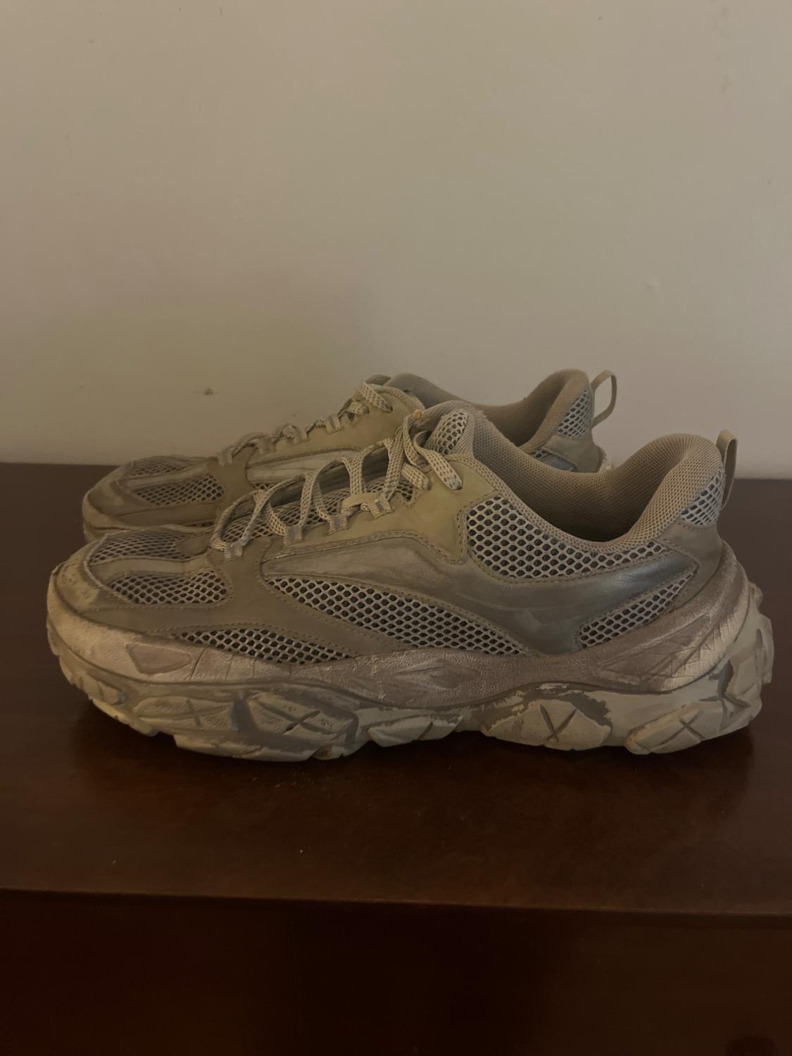 Grey trainers with a chunky sole and mesh detailing, placed on a dark wooden surface.