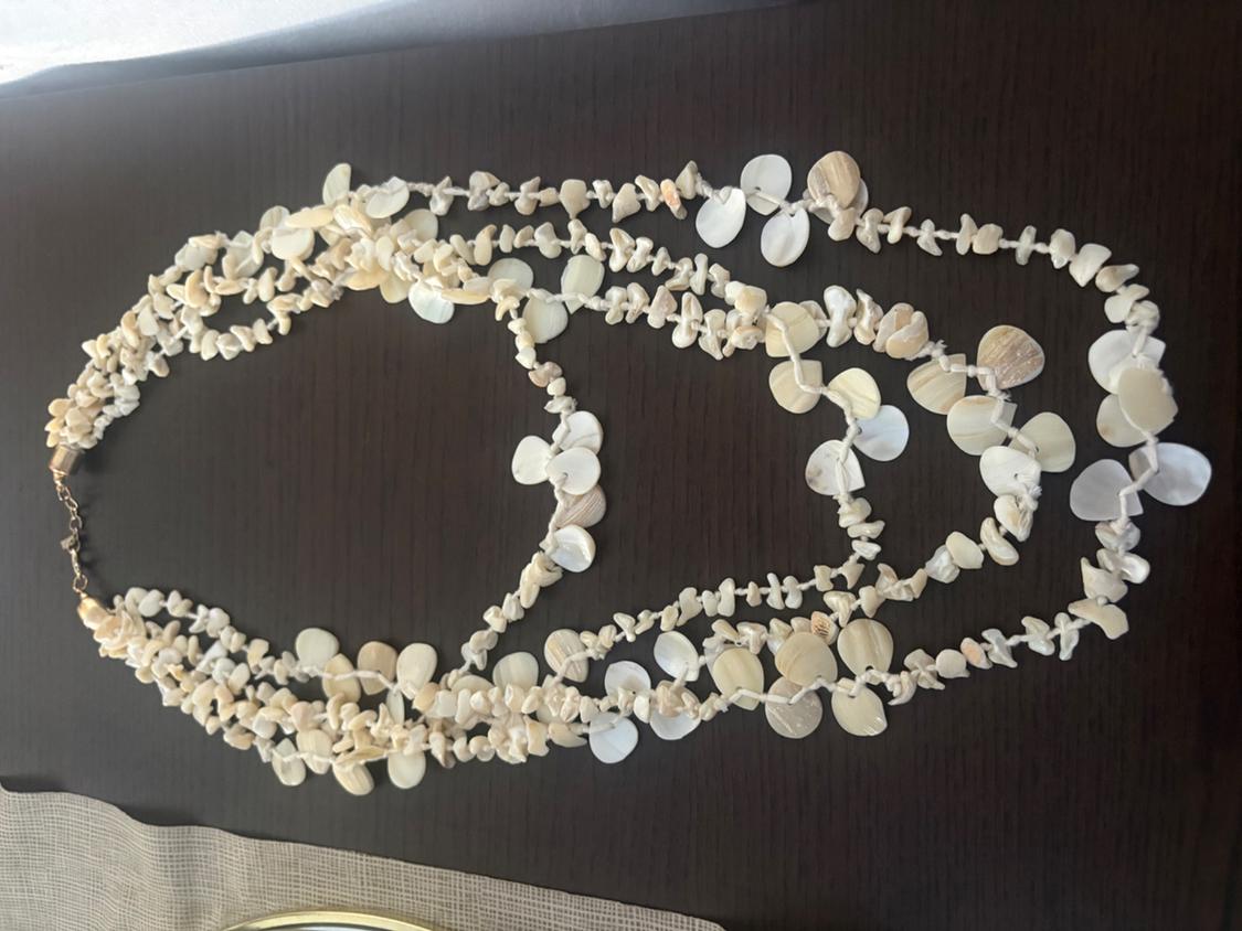 Multi-strand necklace with small shells and round mother-of-pearl pieces in shades of white and ecru, on a dark wood table.